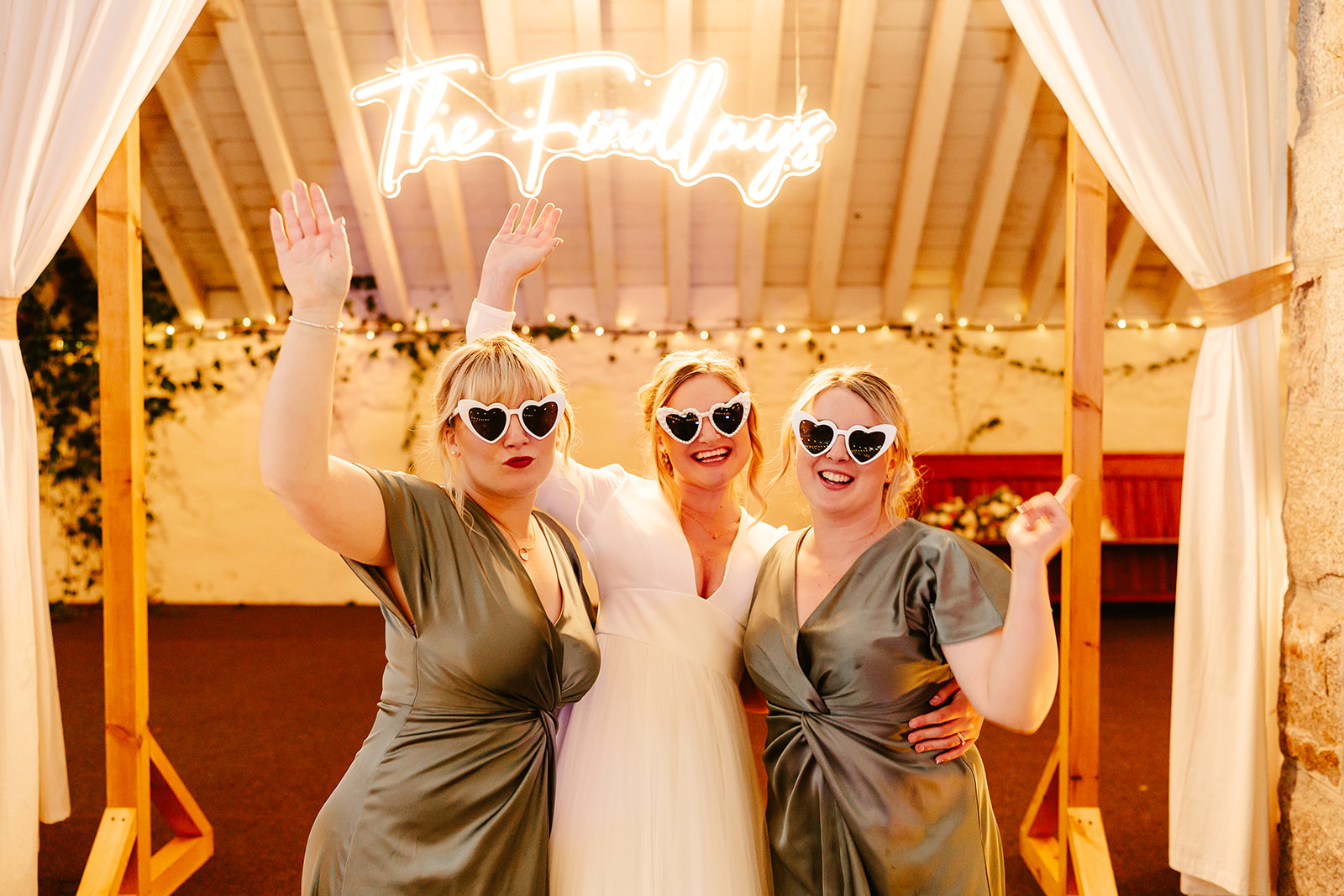 bride and two bridesmaids pose infant of custom neon sign at coos cathedral wedding venue