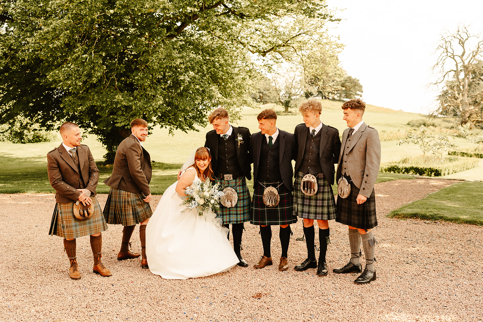 bride and groom pose with men in kilts whilst pulling silly poses with trees behind them