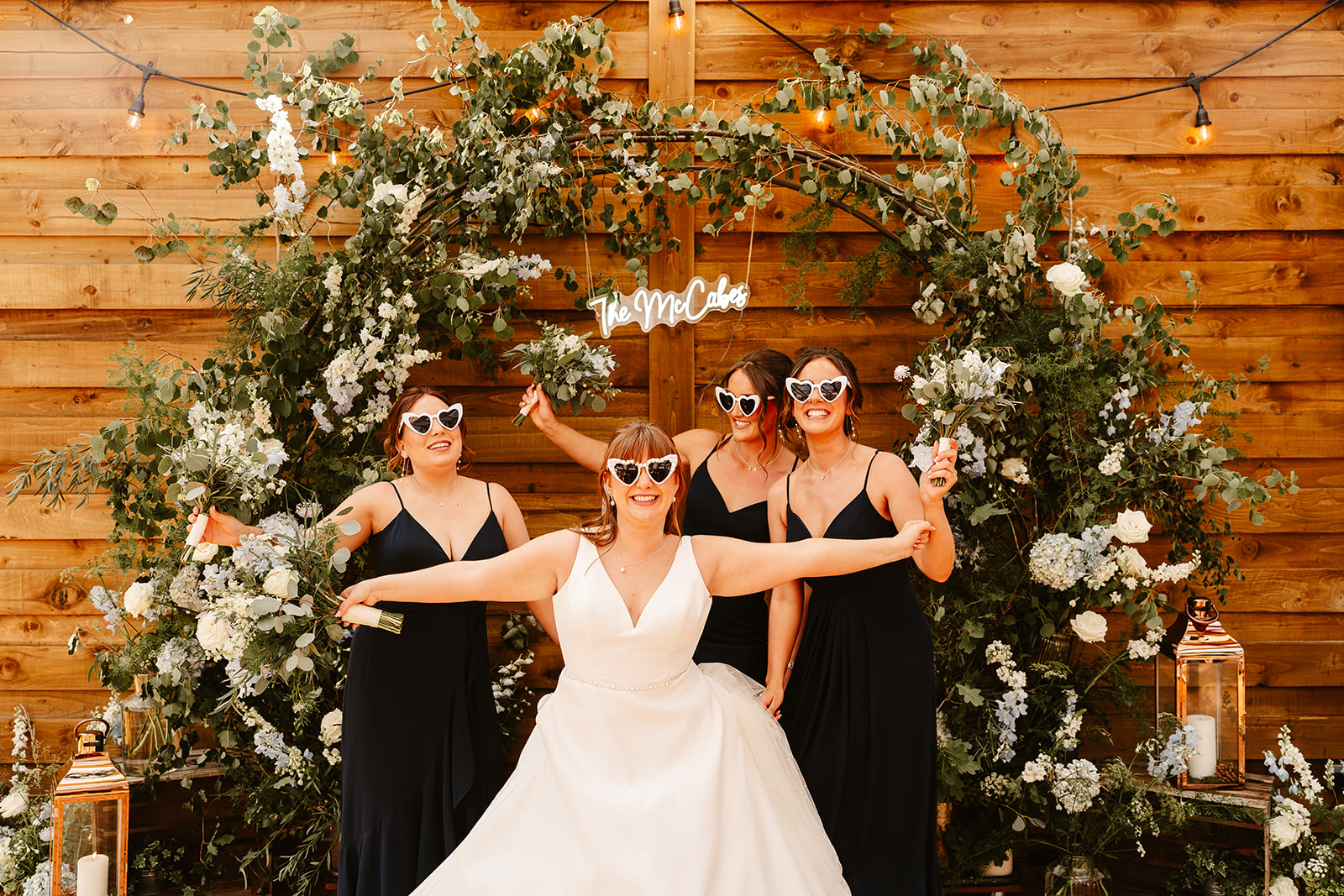 bridal party poses with heart shaped sunglasses on with custom neon sign in the background at Elrick house wedding venue