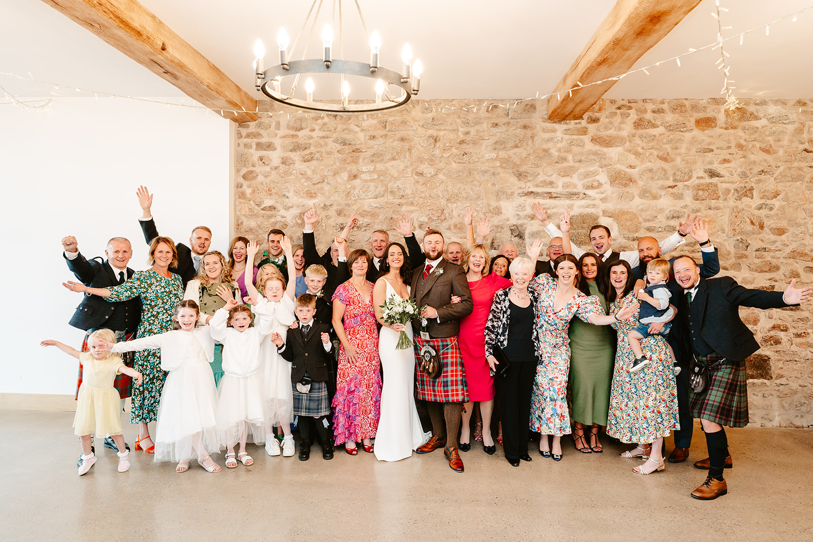 large groups of people pose indoors with hands in air during wedding group shot at Schivas Steading wedding