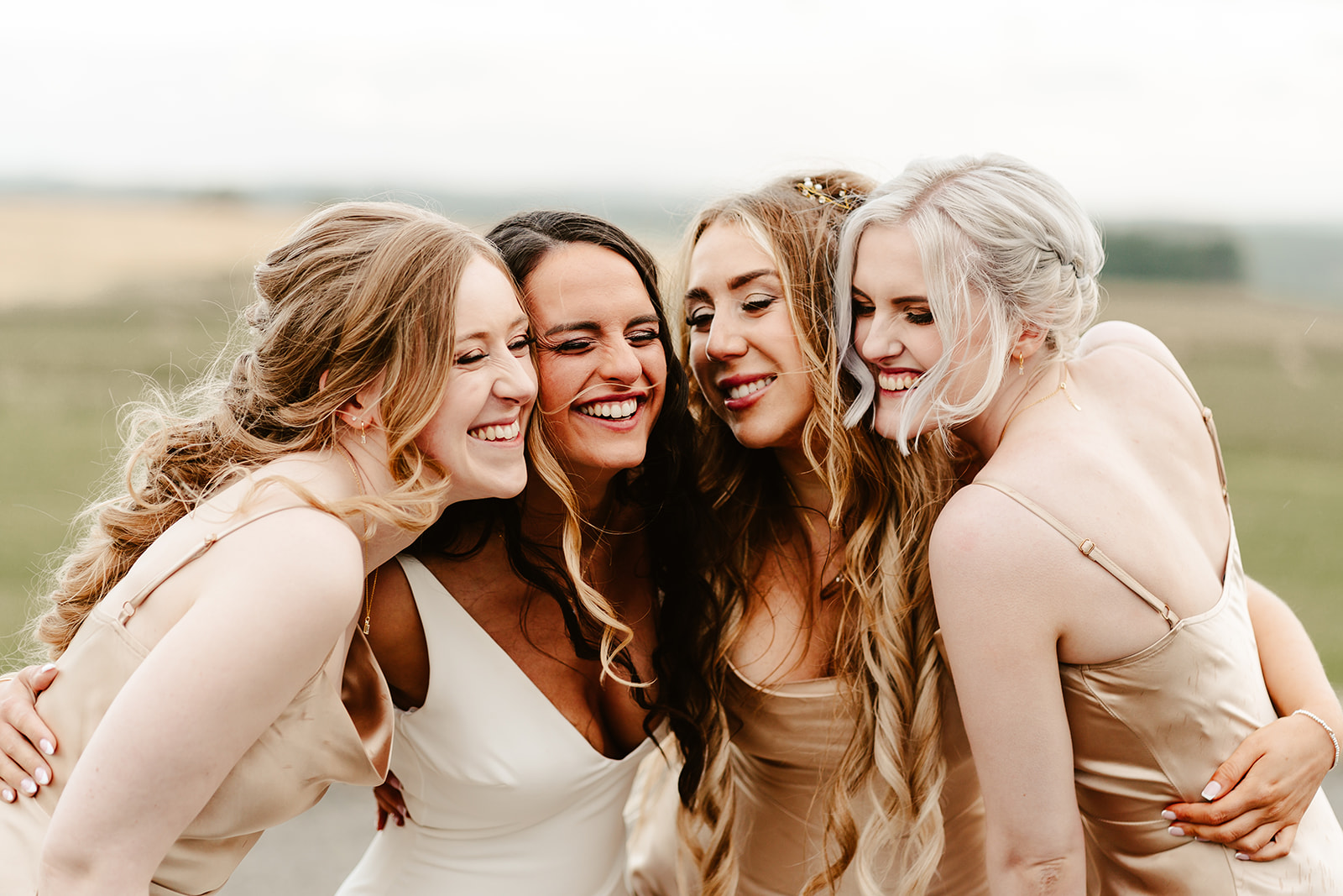 bride and bridesmaids pose cuddled together with views of fields behind them at Schivas Steading wedding
