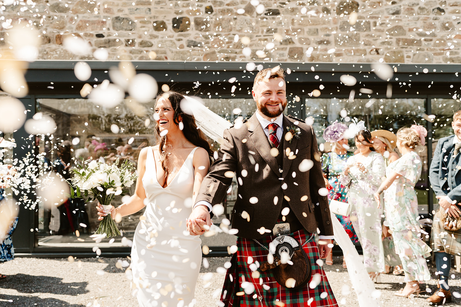 couple walk through falling confetti outdoors during their wedding ceremony at Schivas steading