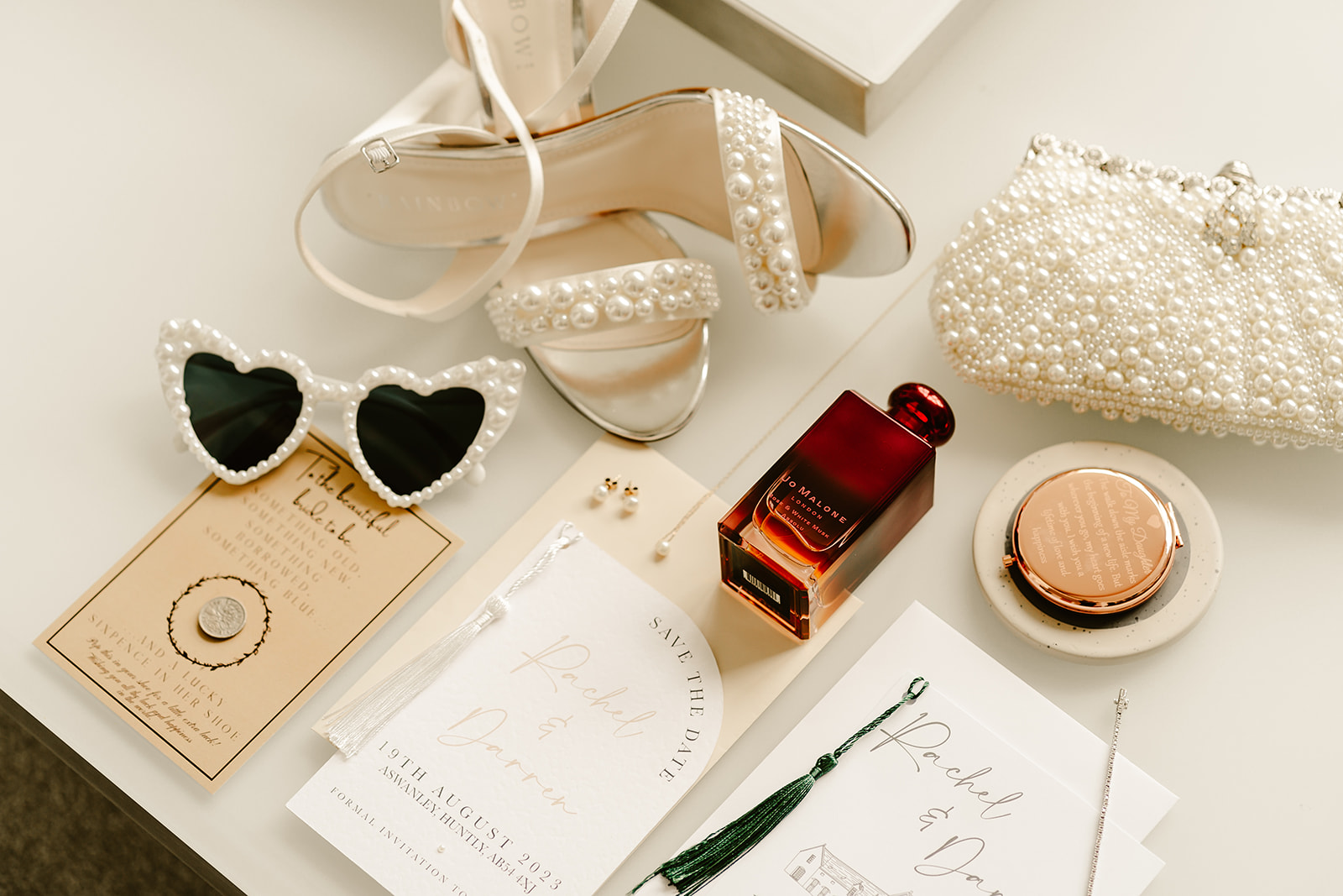 a flat lay photo of brides accessories there is sunglasses perfume shoes and dos cards