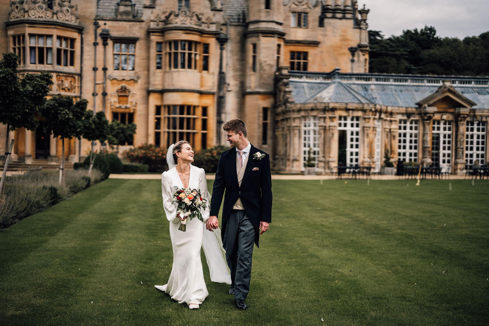 bride and groom walking across the lawns at Harlaxton Manor.