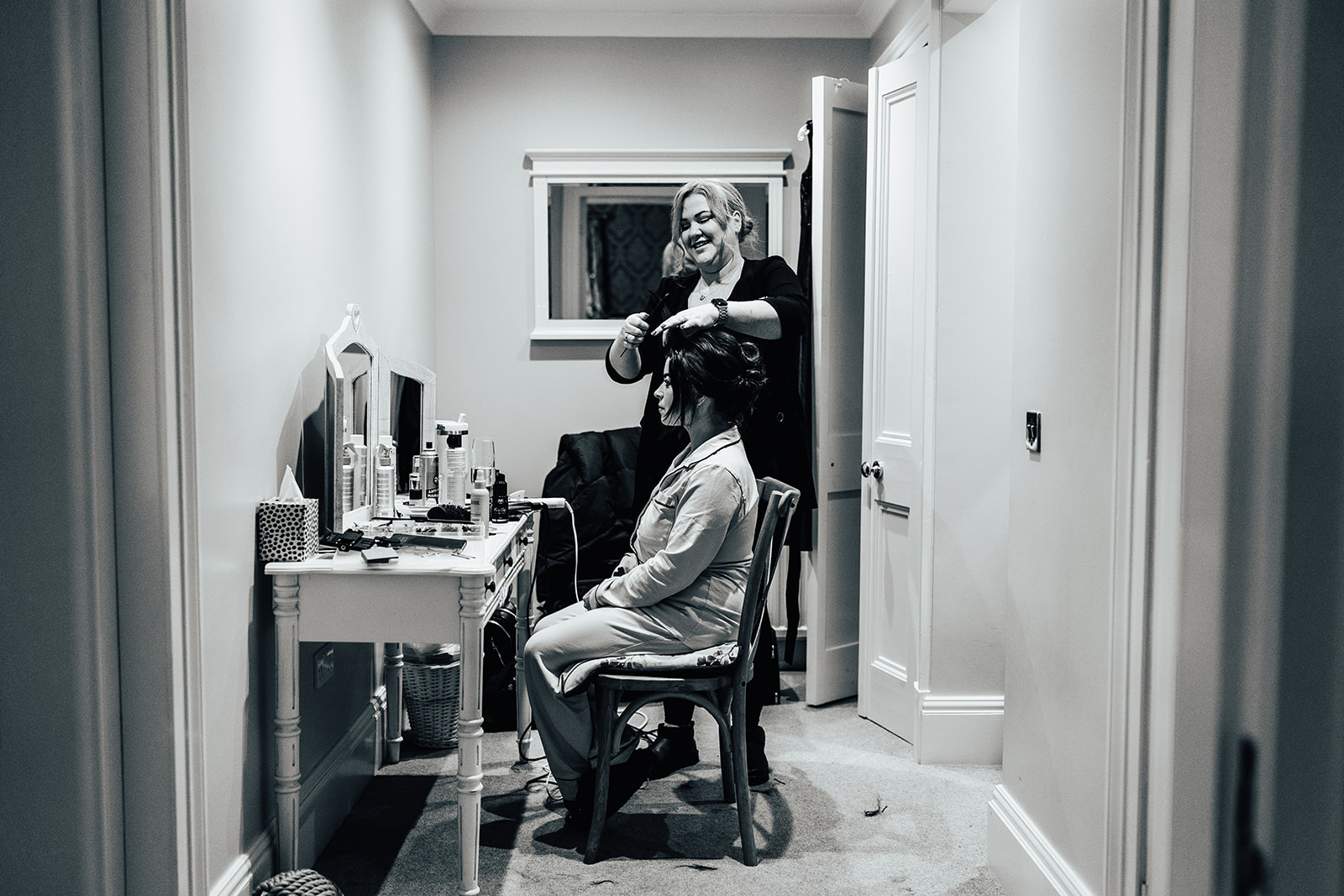 bride is having her hair styled sitting at a vanity table