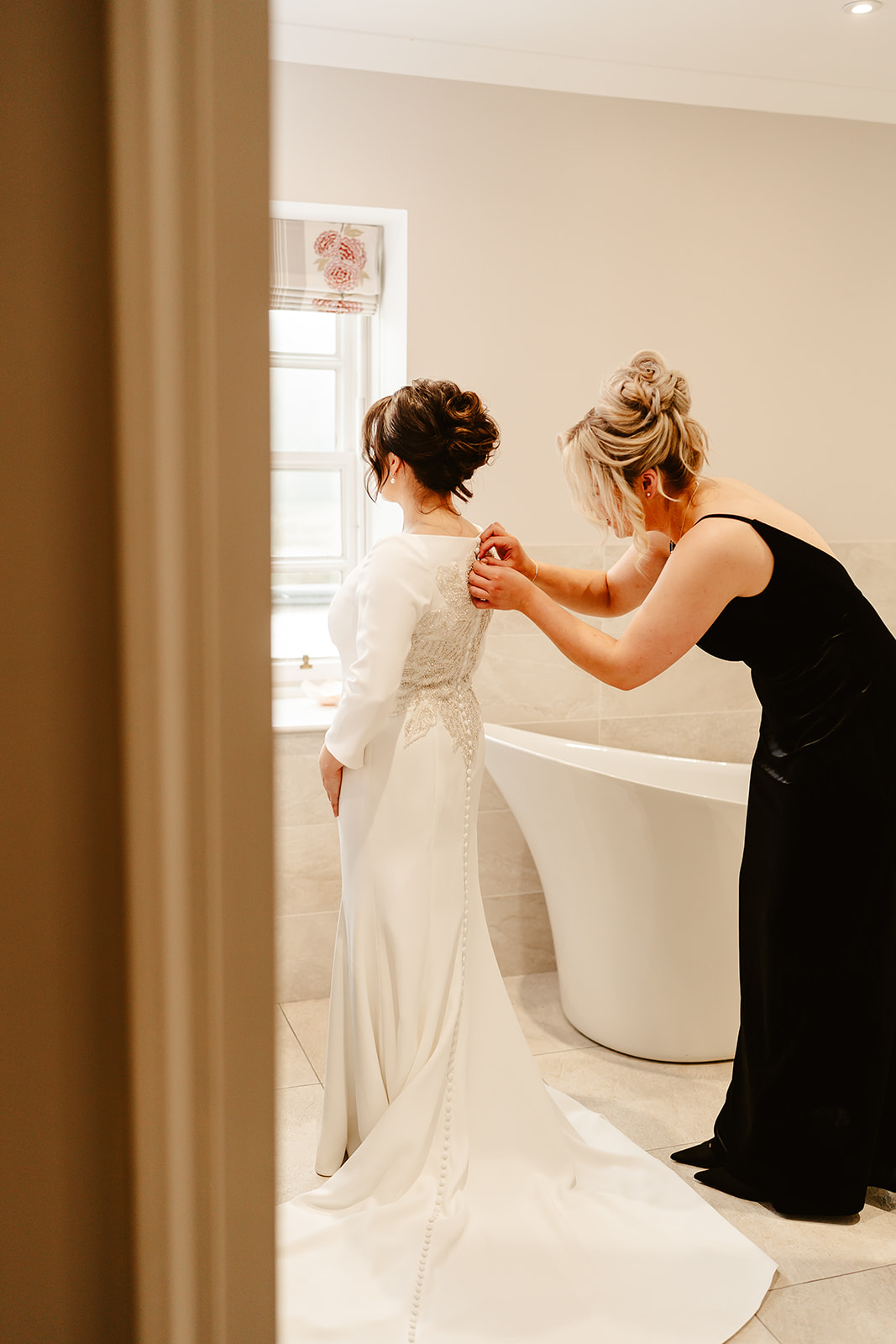 bridemaid helps bride button up the back of her dress at ballogie house