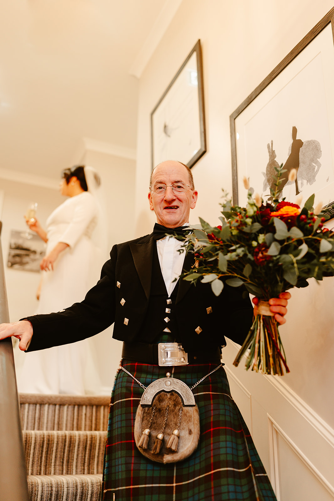 father of the bride is holding wedding flowers as he walks down the stairs