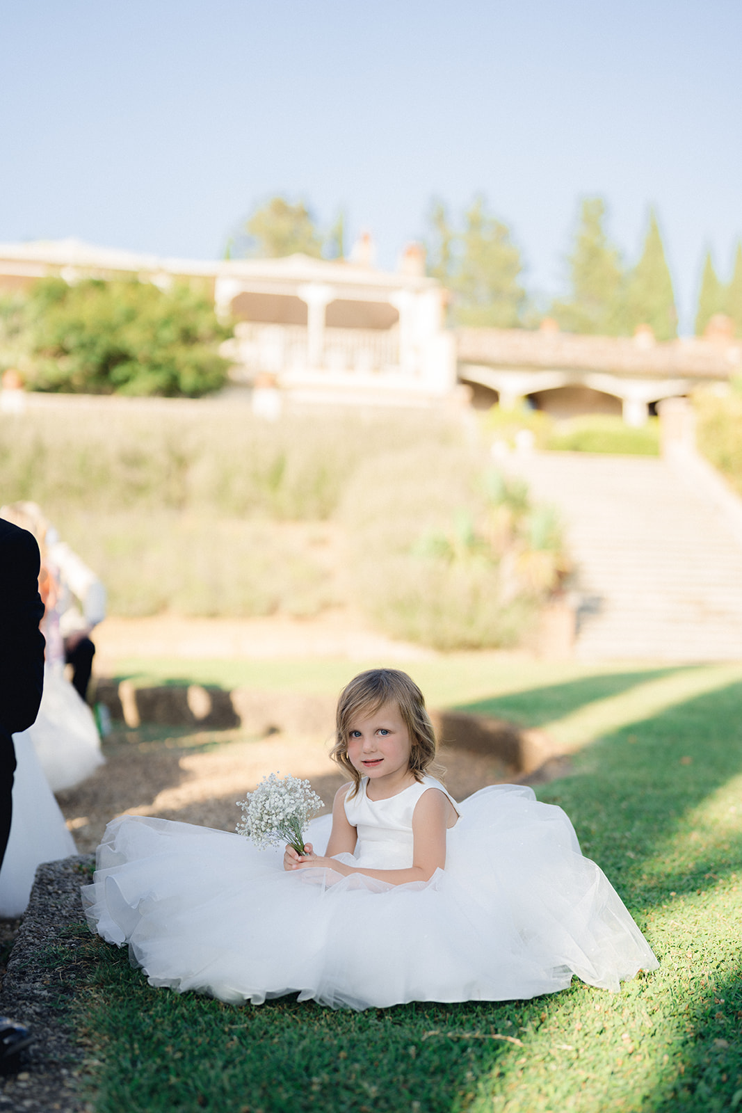 a cute flower girl sitting on the lawn of the villa