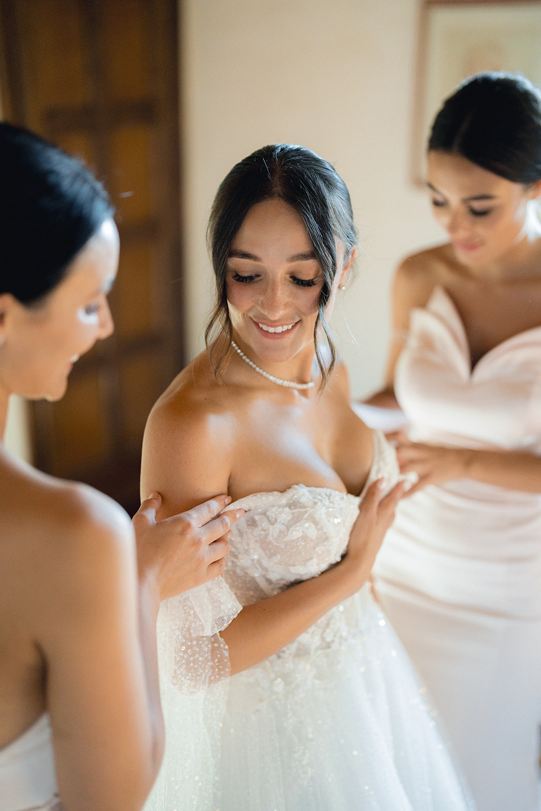 The bride smiles as the bridesmaids help her put on the dress