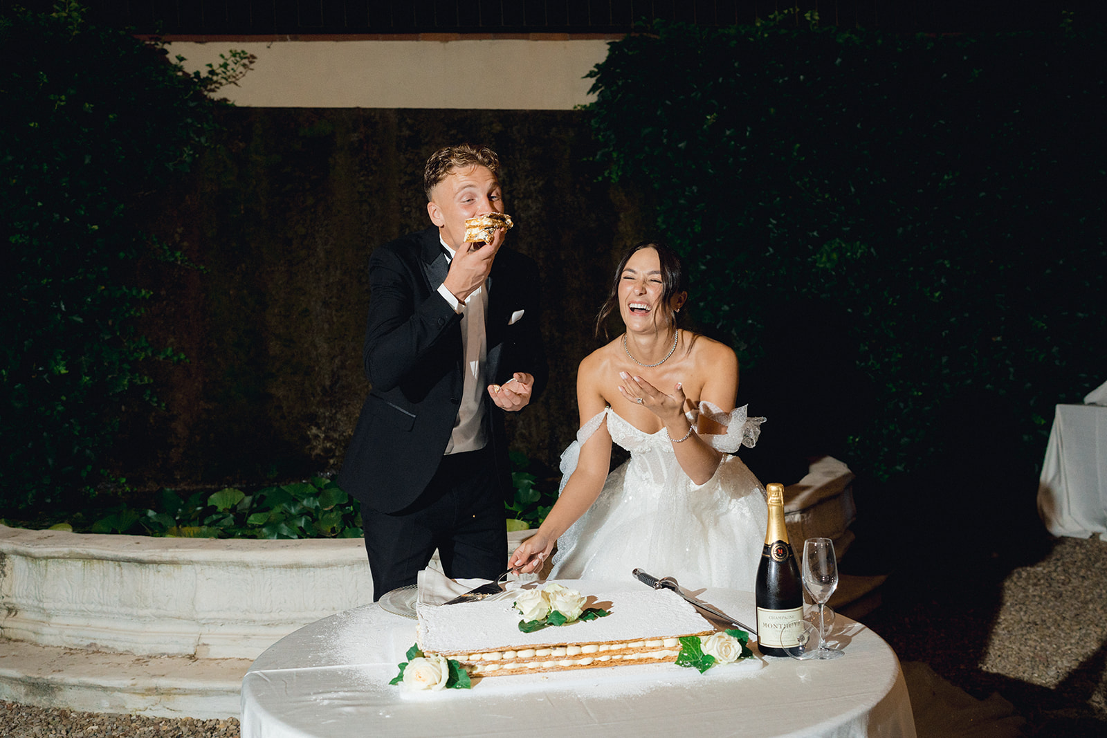The groom tastes the first slice of cake as the bride laughs with delight