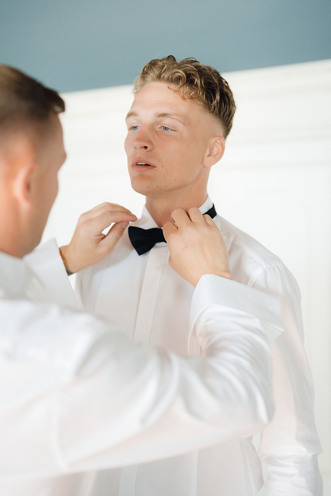 The groom's best man helping him put on the bow tie