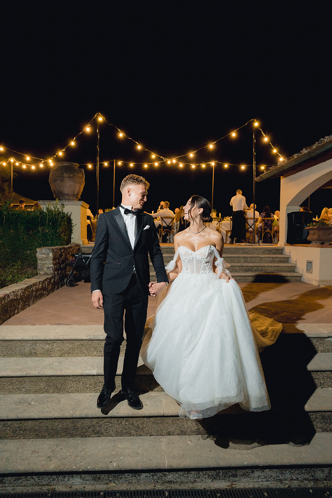 The newlyweds descend the steps of the terrace at Villa La Selva, adorned with Italian lights