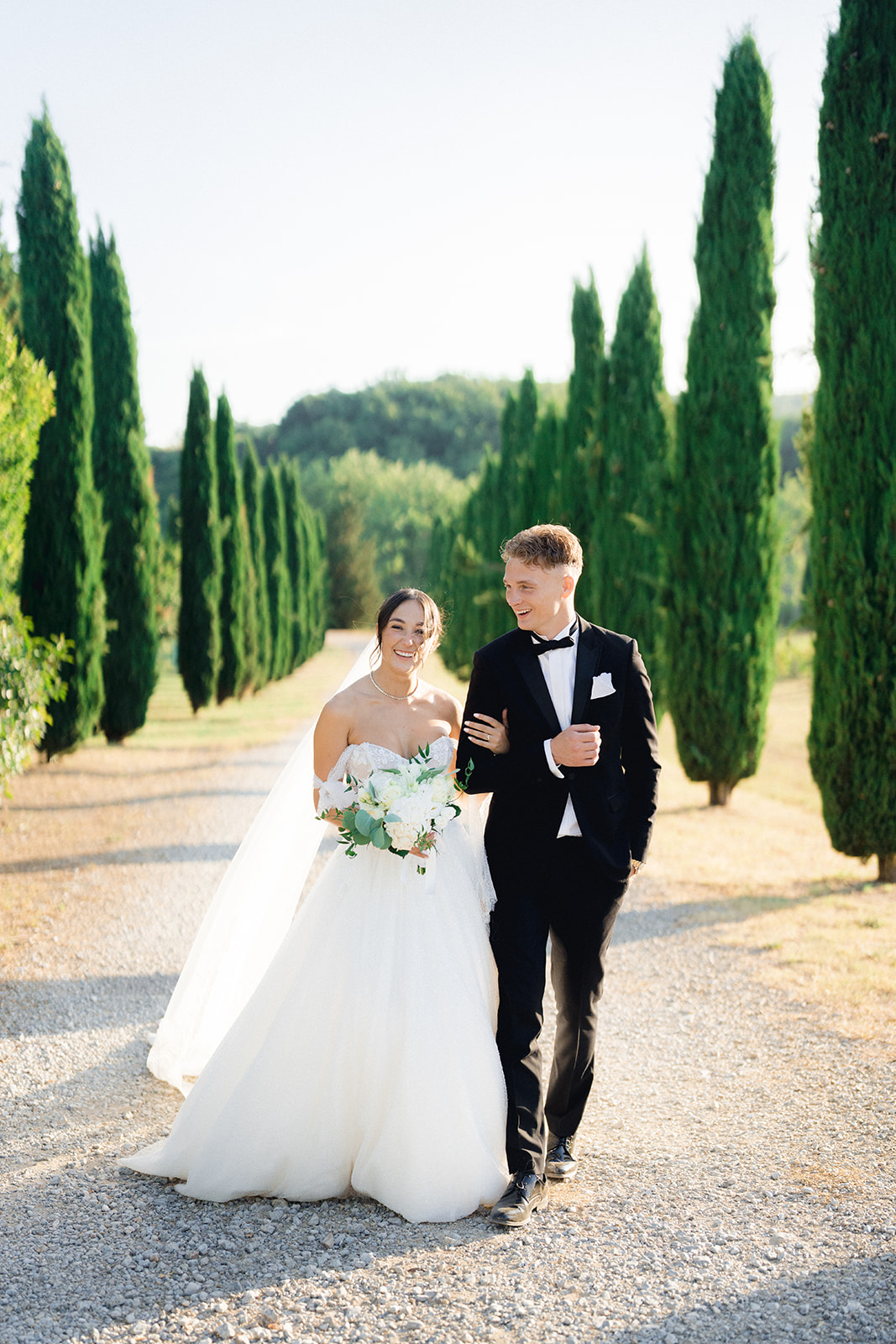 The newlyweds happily walking among the cypress trees near Villa La Selva