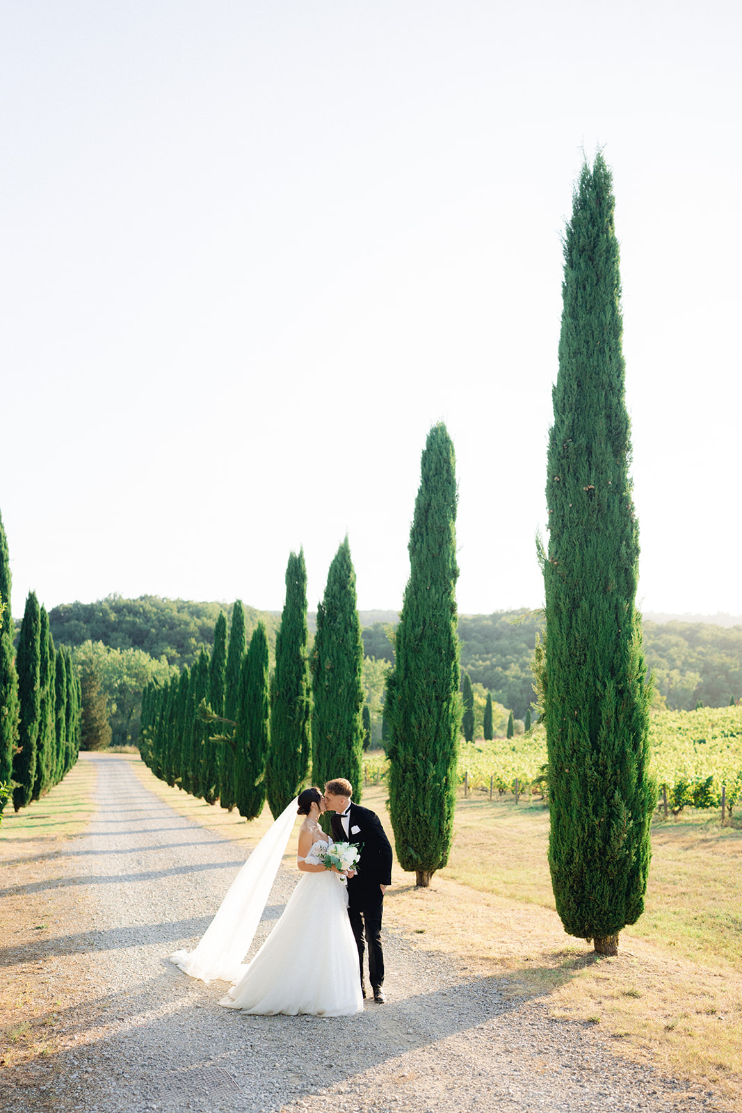 The newlyweds kissing along a cypress-lined avenue in Tuscany