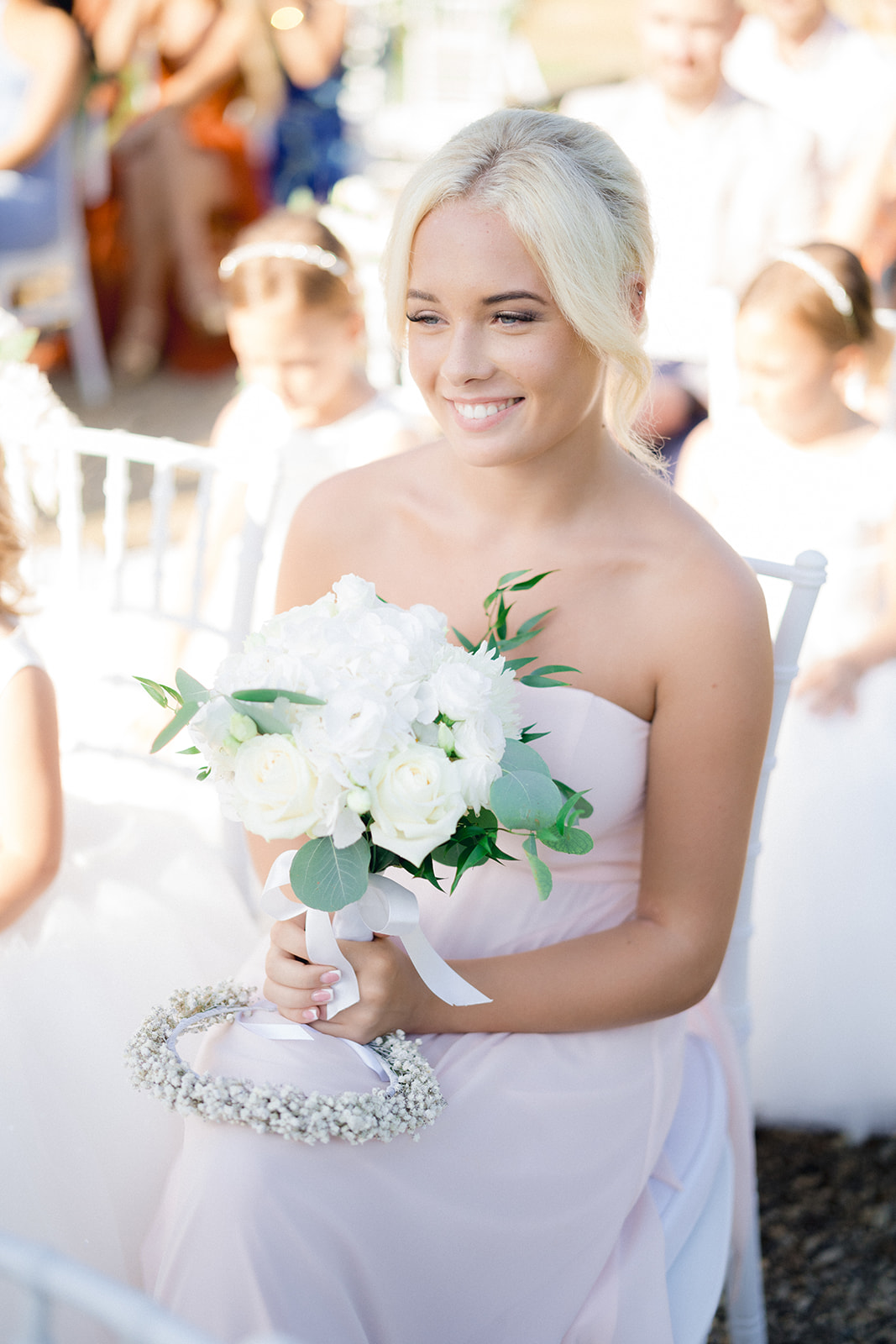 the sister of the groom in a pastel pink dress holding a bouquet of flowers