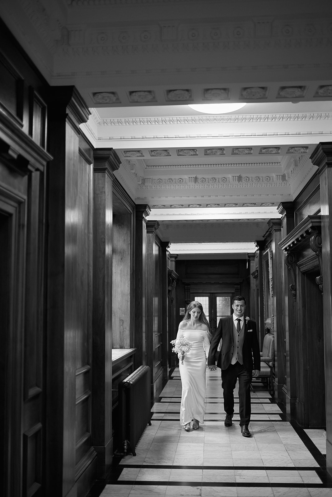 bride and groom hold hands in the hall way