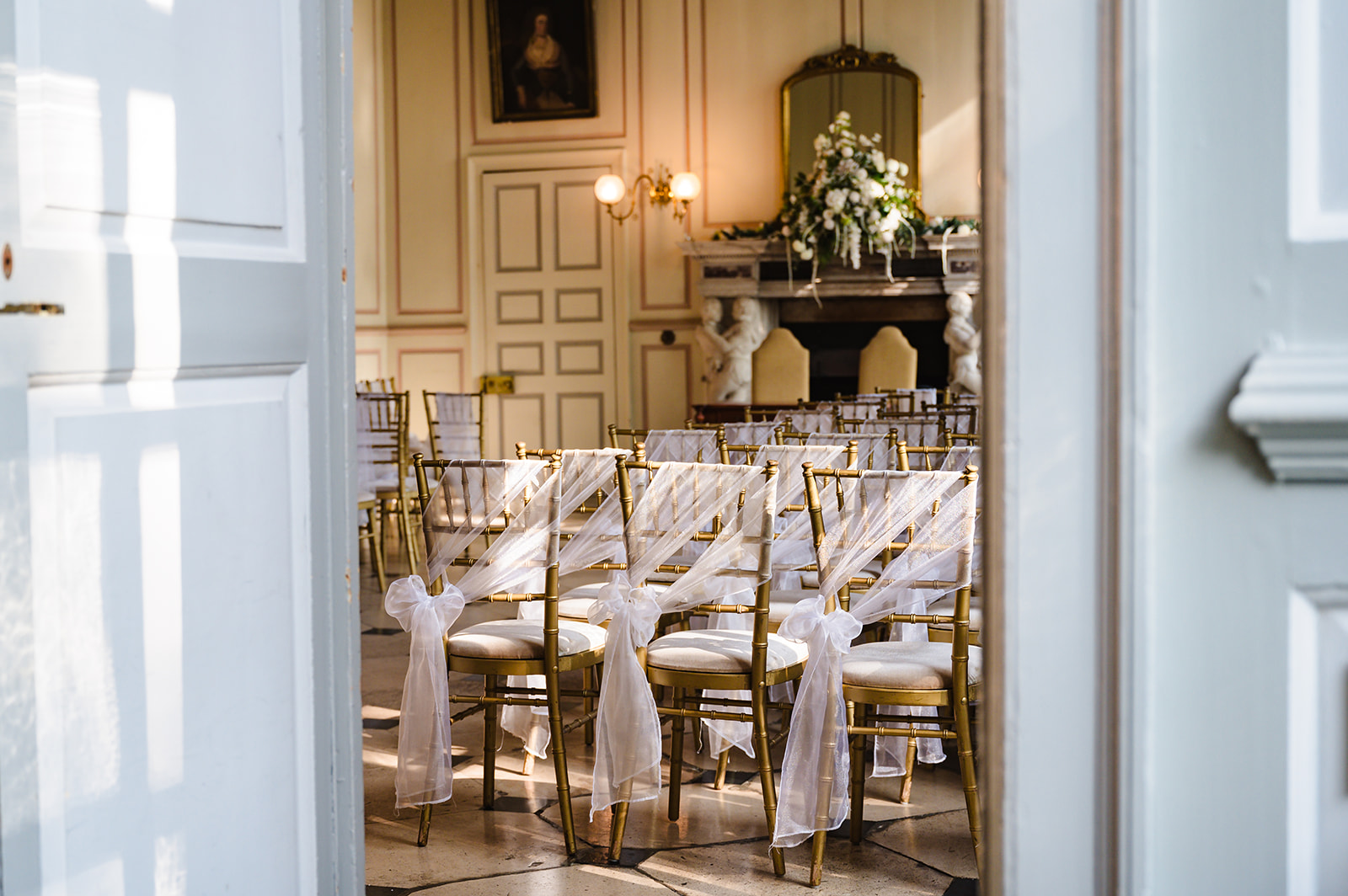 The ceremony room at Gosfield hall with white chair sashes and white and green florals