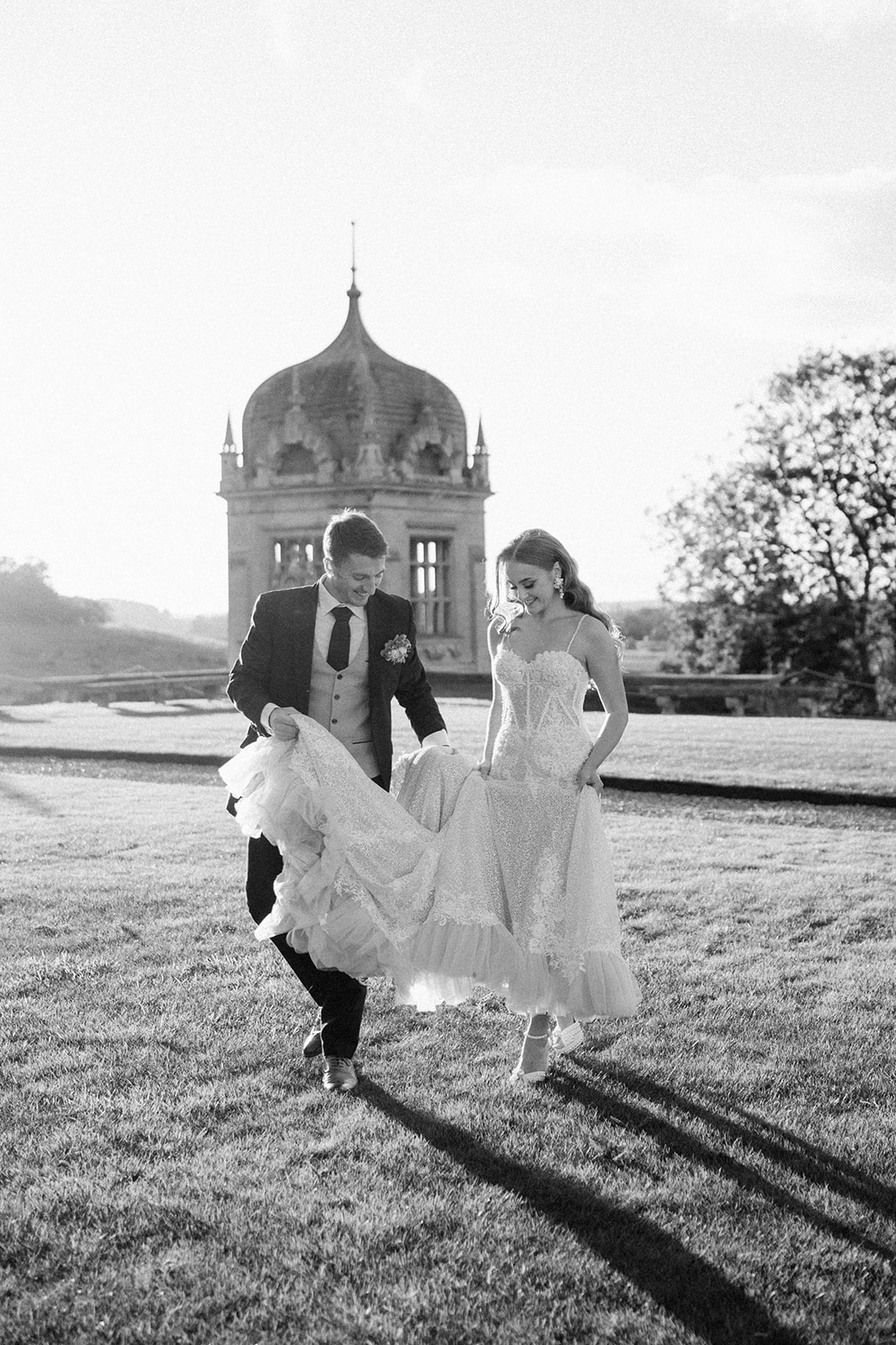 bride and groom walking on grass at golden hour outside harlaxton manor