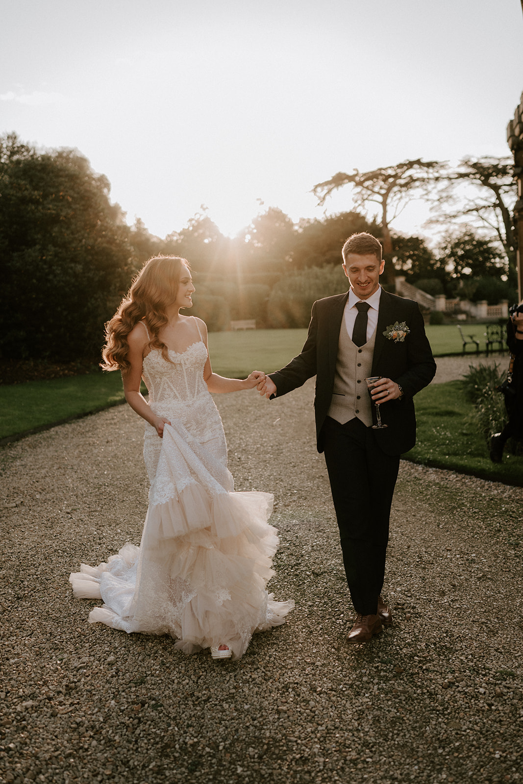 bride and groom walking with sunset behind them at harlaxton manor