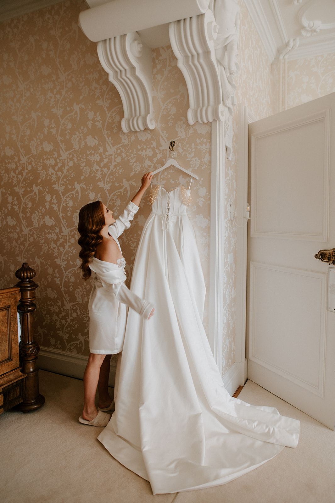 bride reaching up to take wedding dress off hanger