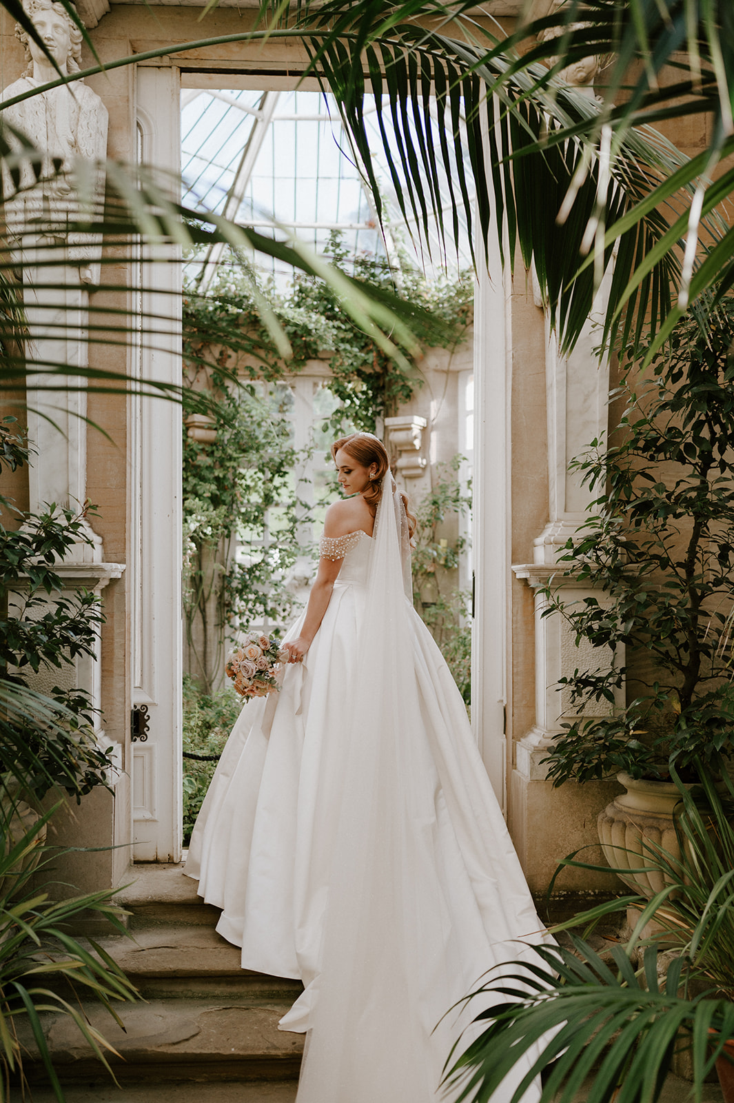 bride standing on step in conservatory at harlaxton manor with dress falling down