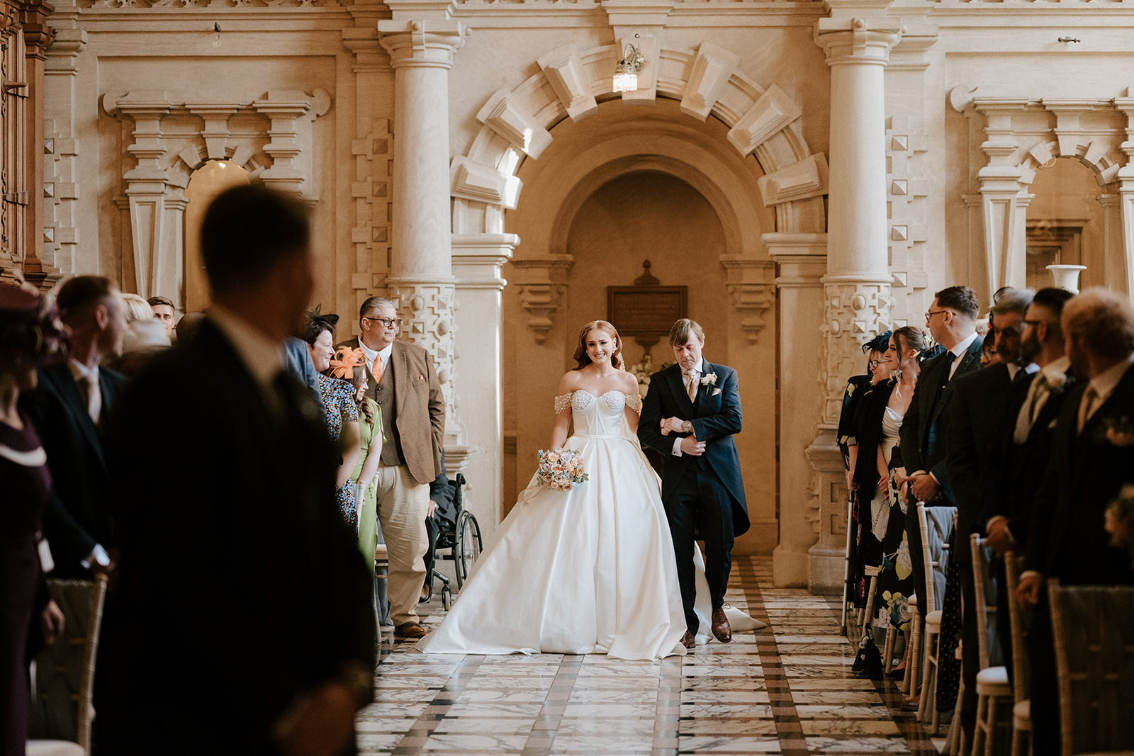 bride walking down the aisle in the great hall at harlaxton manor