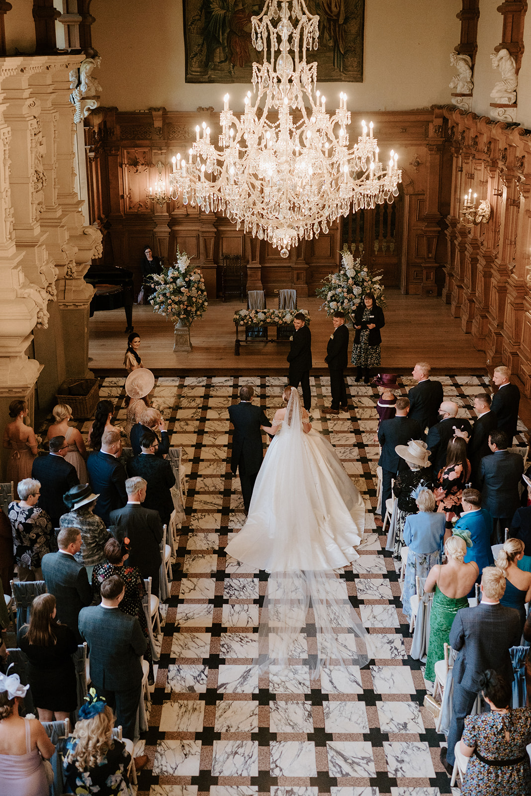 bride walking down the aisle in the great hall at harlaxton manor