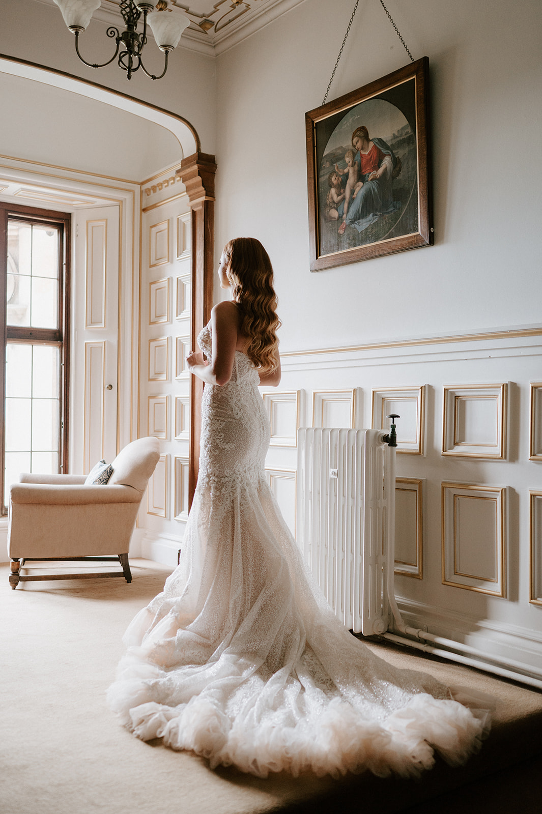bride wearing wedding dress looking out of window at harlaxton manor