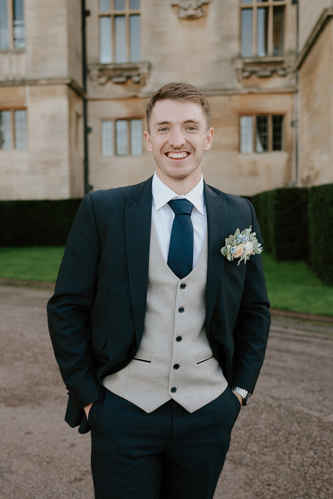 groom in blue suit smiling outside harlaxton manor