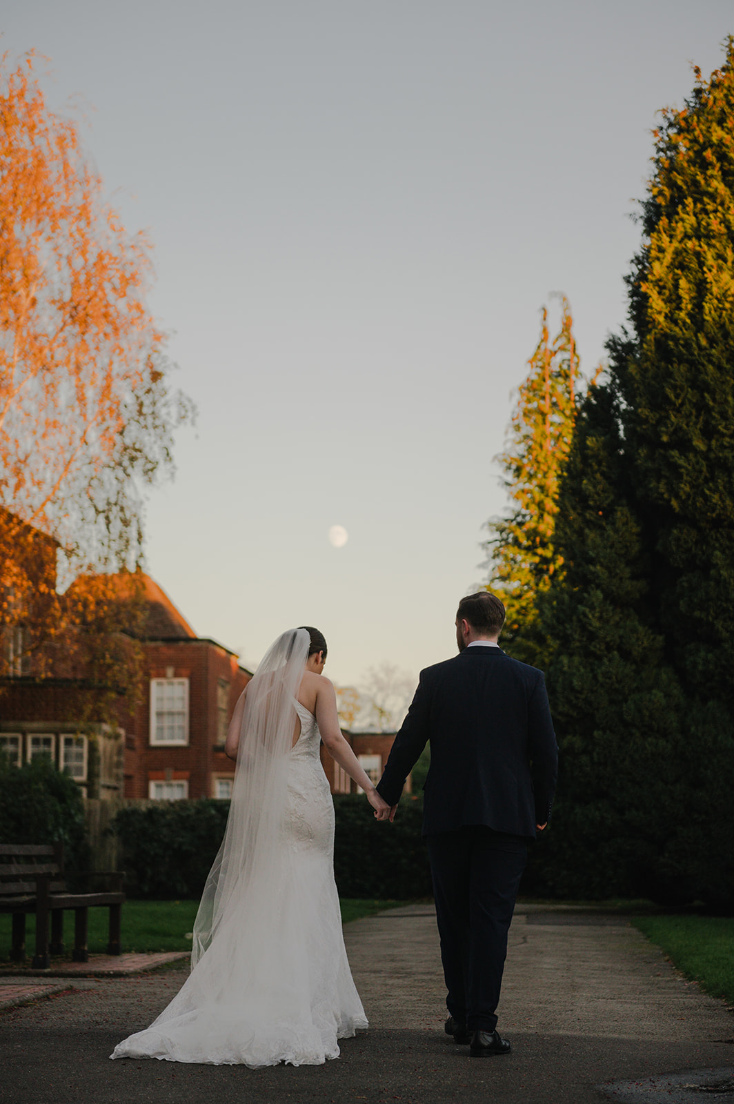 the bride and groom walking in the garden at highbury hall with the moon in the sky above them