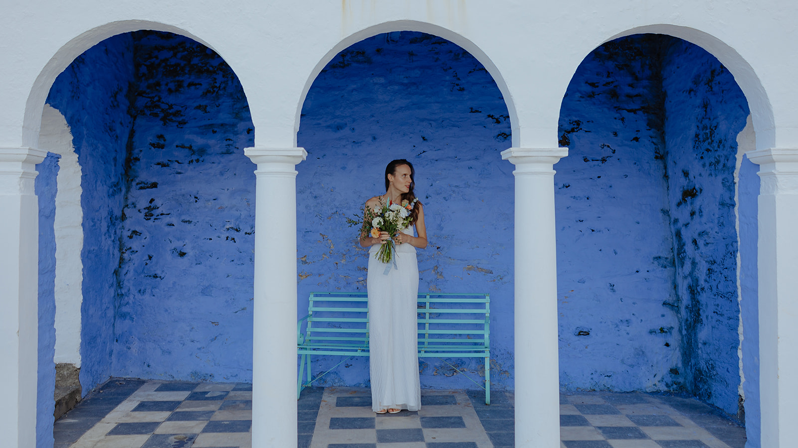 bride under arches with blue wall at Frances quinn wedding in wales