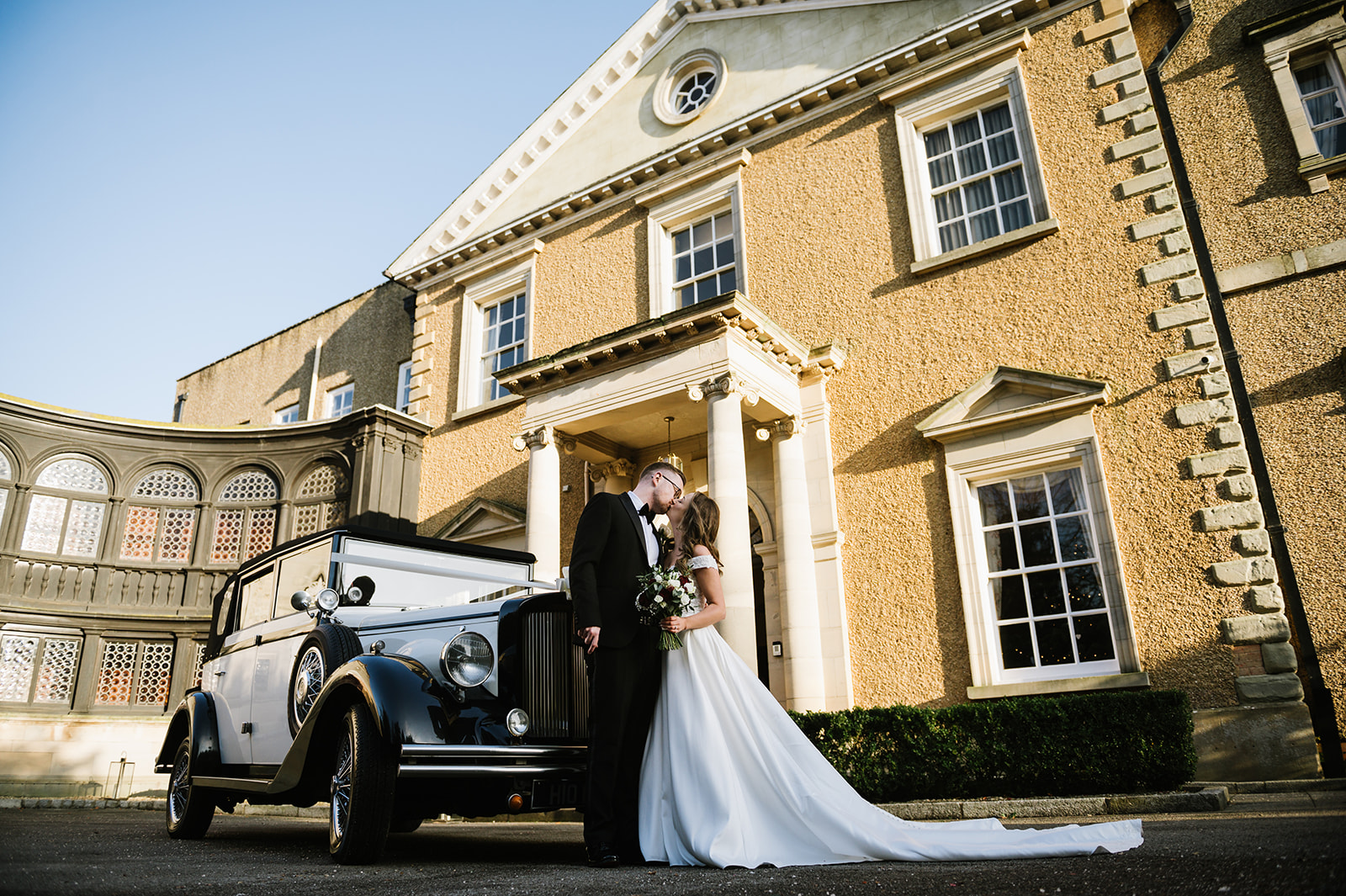 the bride and groom kiss outside Bourton Hall next to their wedding car