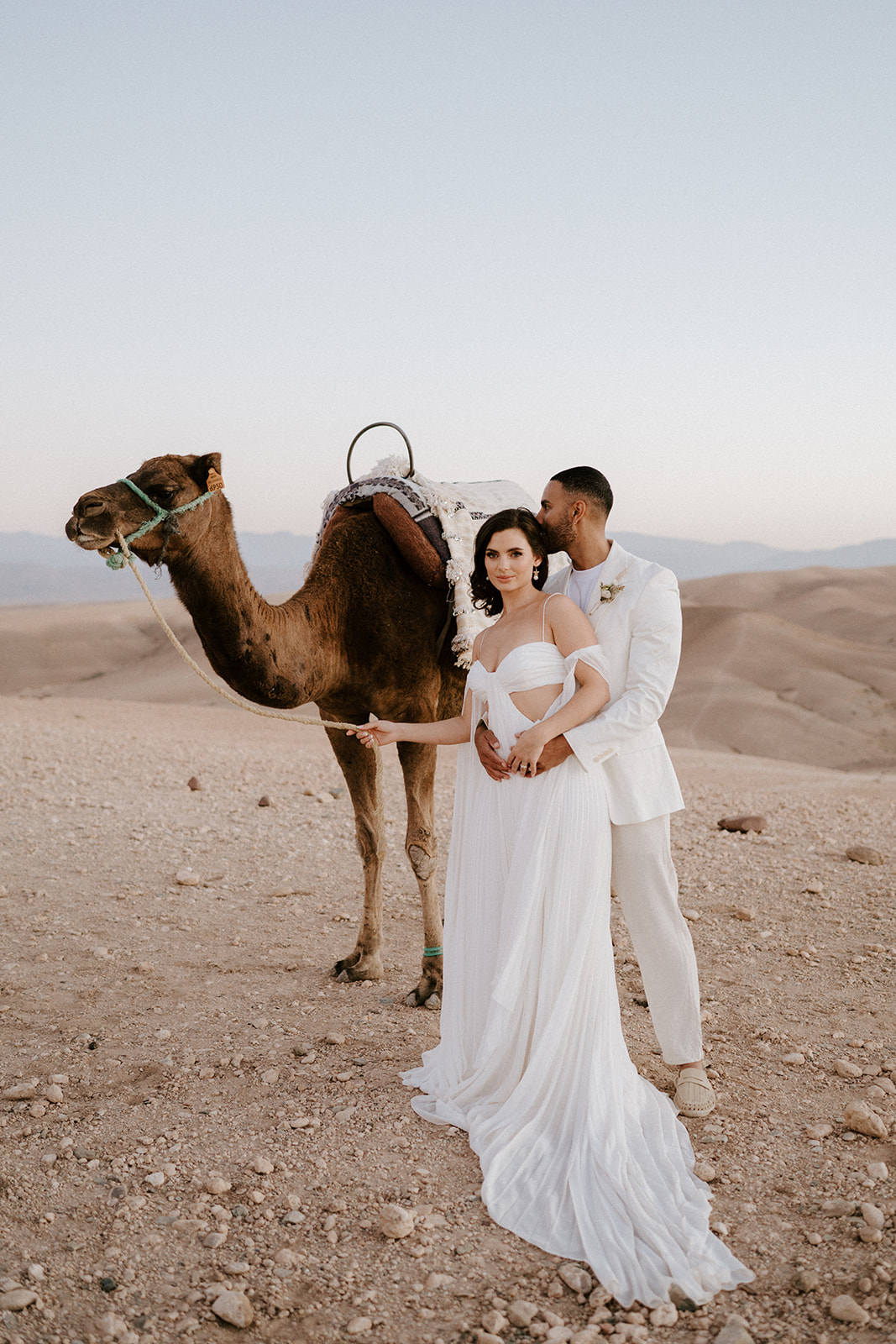 bride and groom standing next to camel after eloping in agafay desert