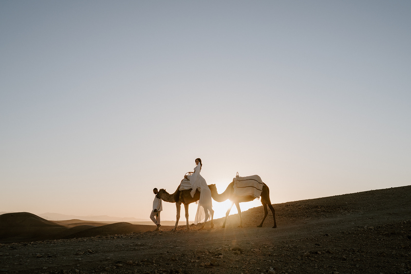 bride on camel walking with groom at agafay desert in marrakesh at sunset