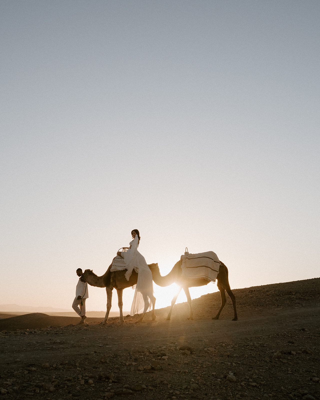 bride on camel walking with groom in agafay desert at sunset