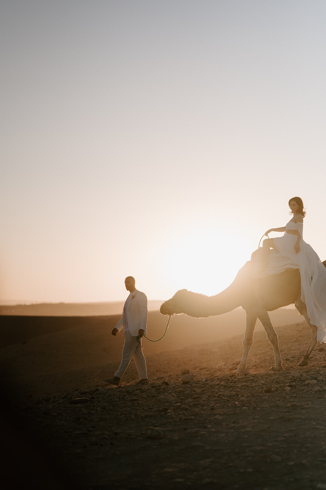 bride on camel walking with groom in agafay desert at sunset