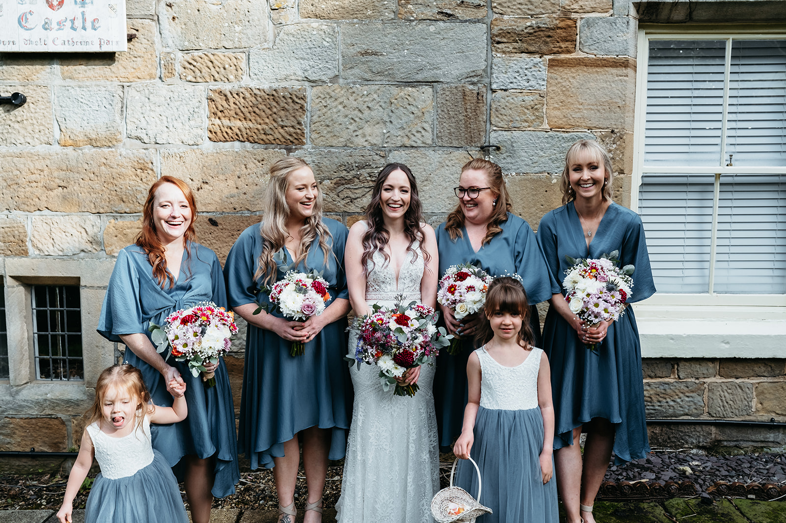 A joyful group photo featuring Adelle, and their wedding party, posing together in front of the stunning danby castle