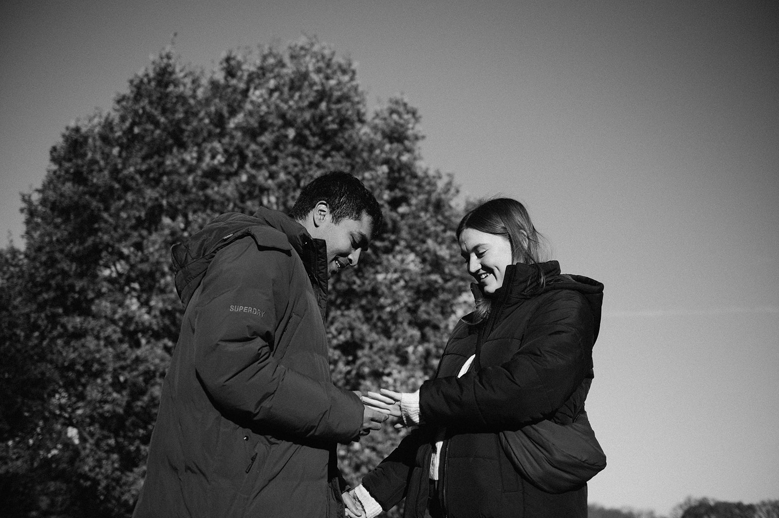 Couple in black and white wearing winter coats looking at her engagement ring.