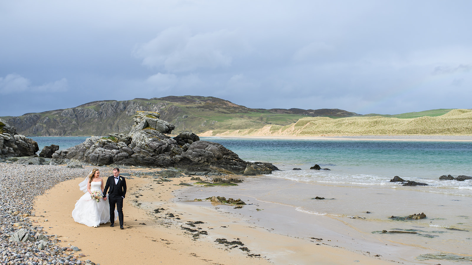 Couple walking across beach at the Isle of Doagh on their Wedding Day
