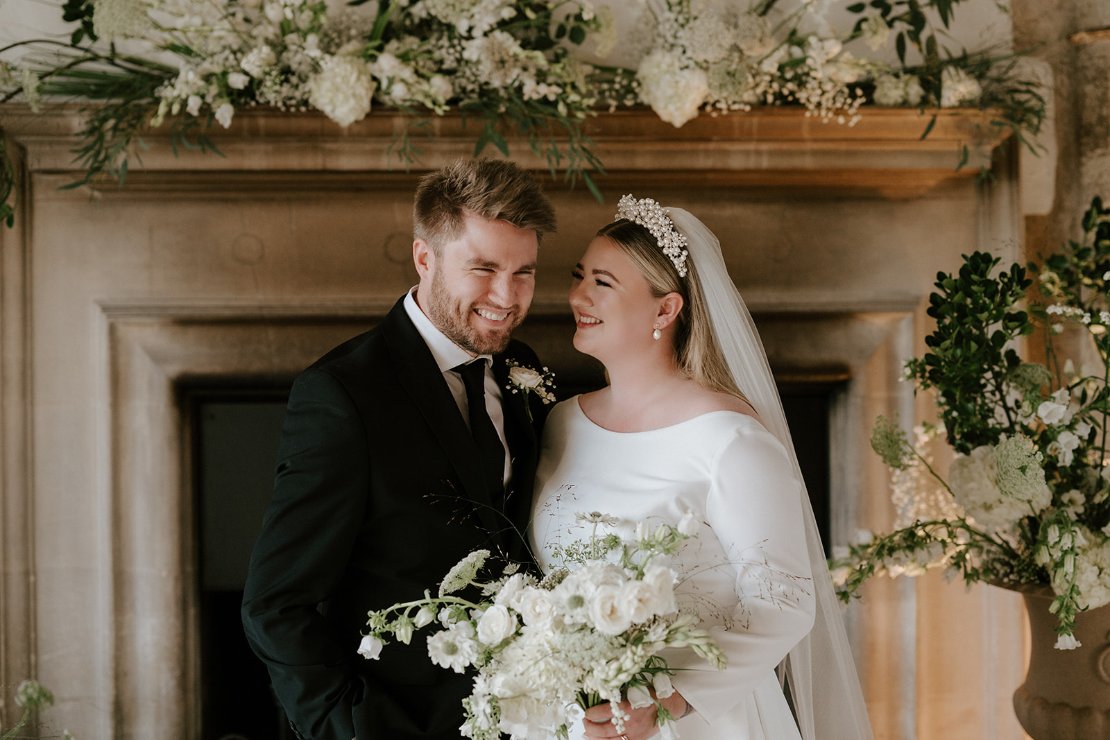 bride and groom against floral mantlepiece backdrop in great hall at butley priory
