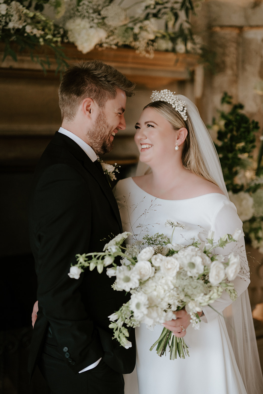 bride and groom against floral mantlepiece backdrop in great hall at butley priory