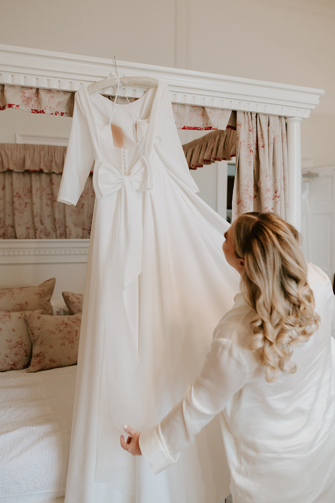 bride playing with dress that's hanging up on four poster bed in bridal suite at butley priory