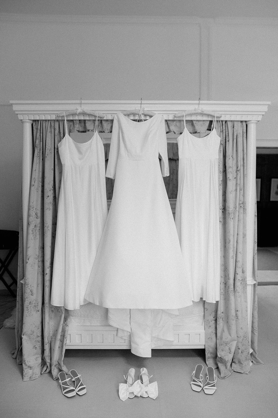 wedding dress hanging with bridesmaid dresses on four poster bed at butley priory