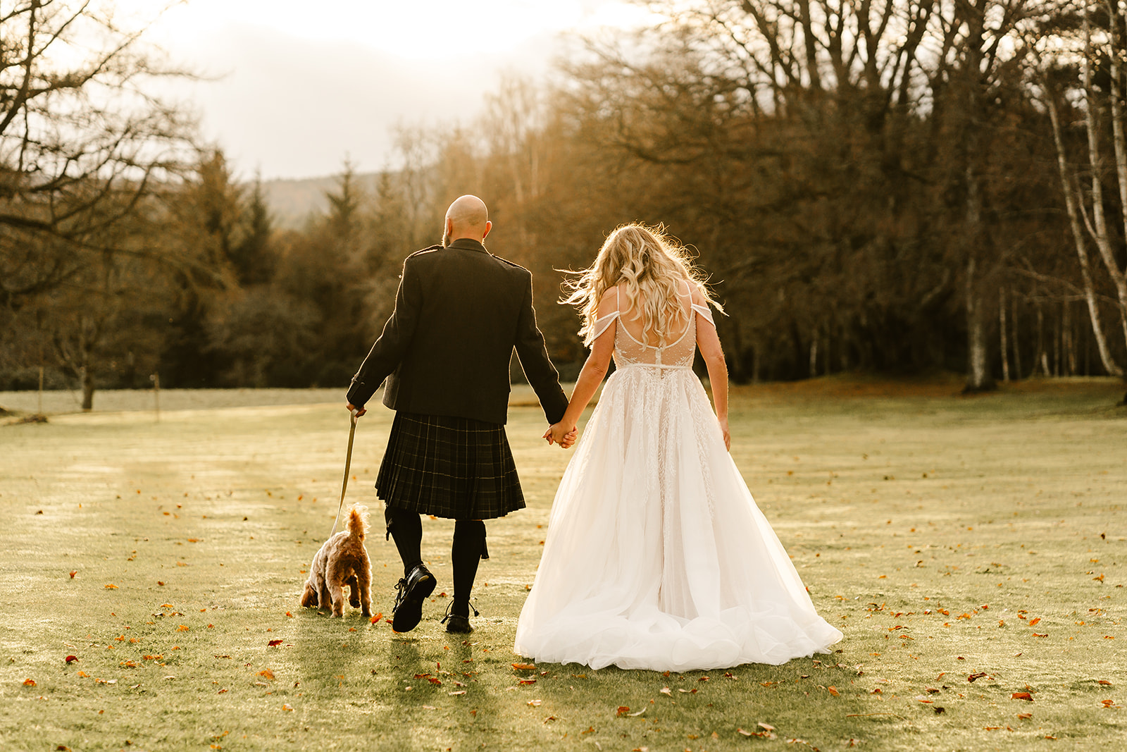 bride and groom walk with the dog on the grounds of raemoir house the sun in shining behind them