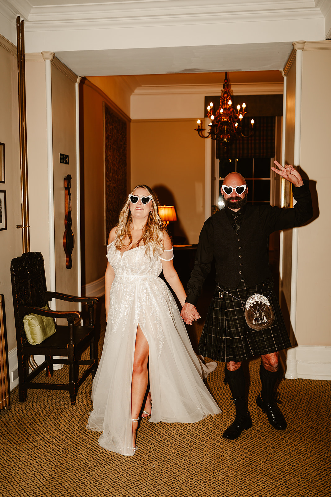 bride and groom walking through the hall of raemoir house posing with heart shaped sunglasses on