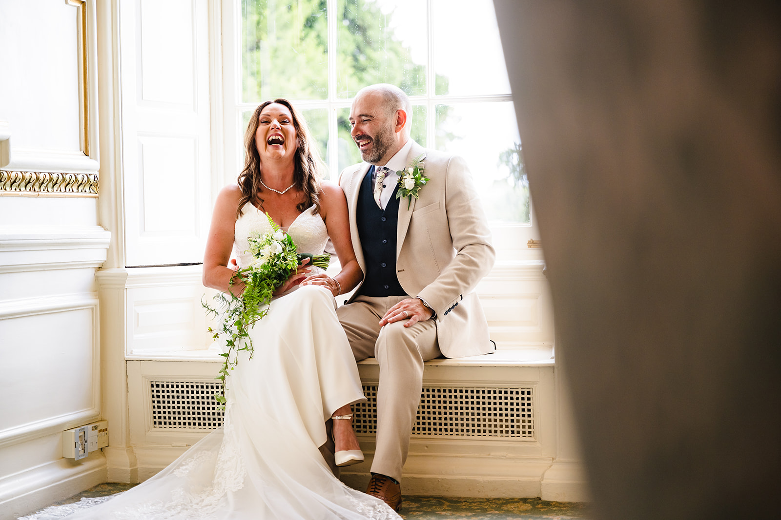 Bride and groom sat on windowsill laughing after their wedding at Stapleford Park Hotel by Amanda Forman Photography