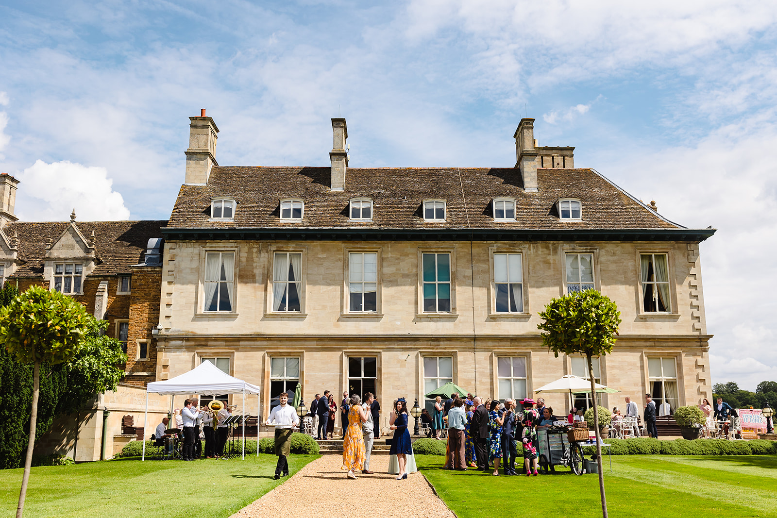The back of Stapleford park showing the gardens and terrace are with wedding guests by Amanda Forman Photography