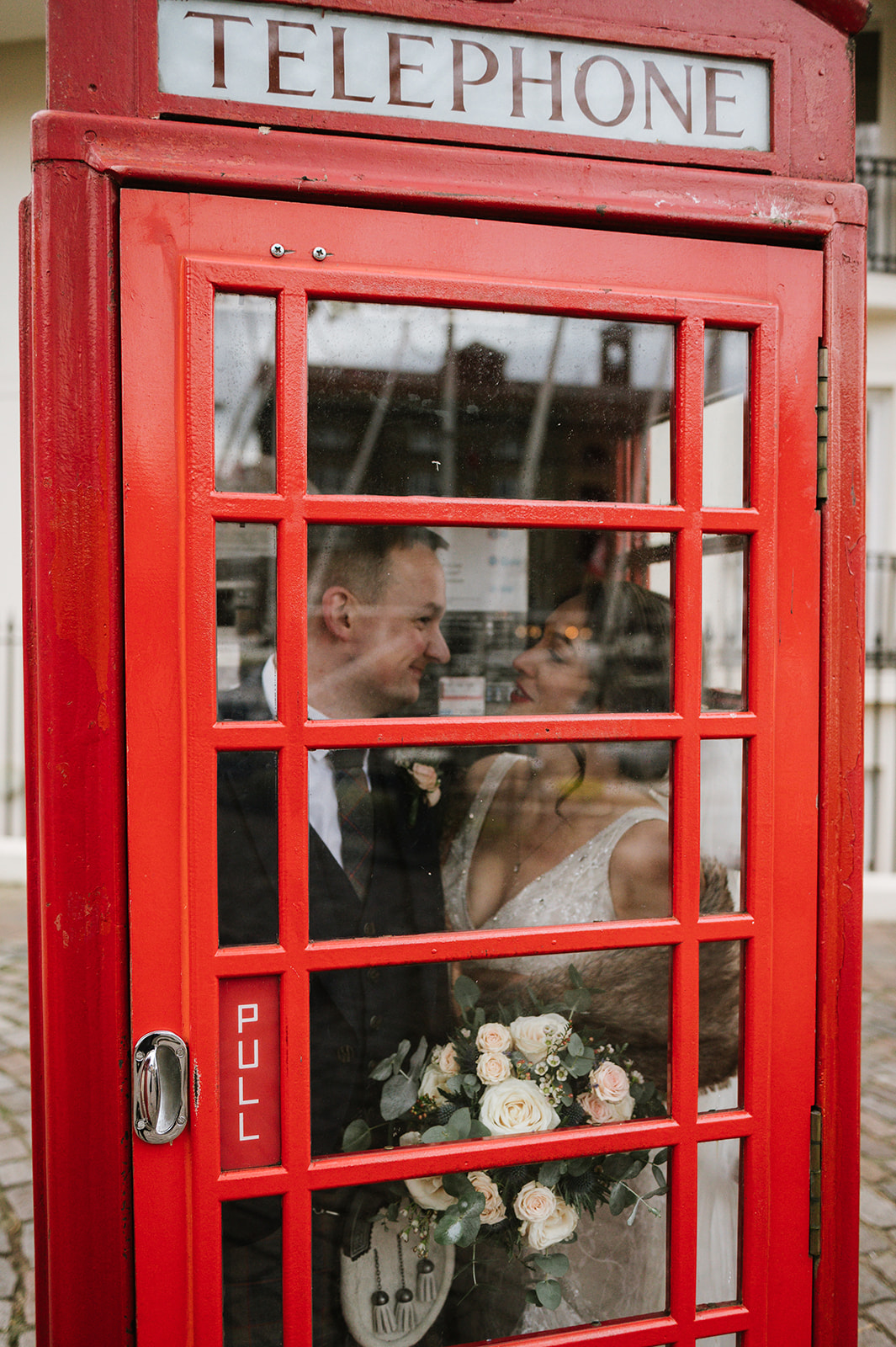 Bride and groom in a red phone box in London outside Dickens Inn on their wedding day