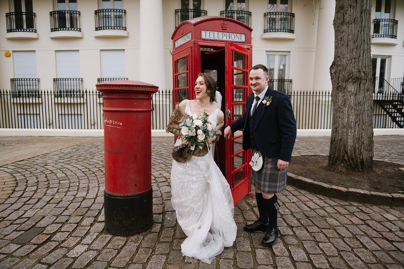 Bride and groom in a red phone box next to a post box in London outside Dickens Inn on their wedding day