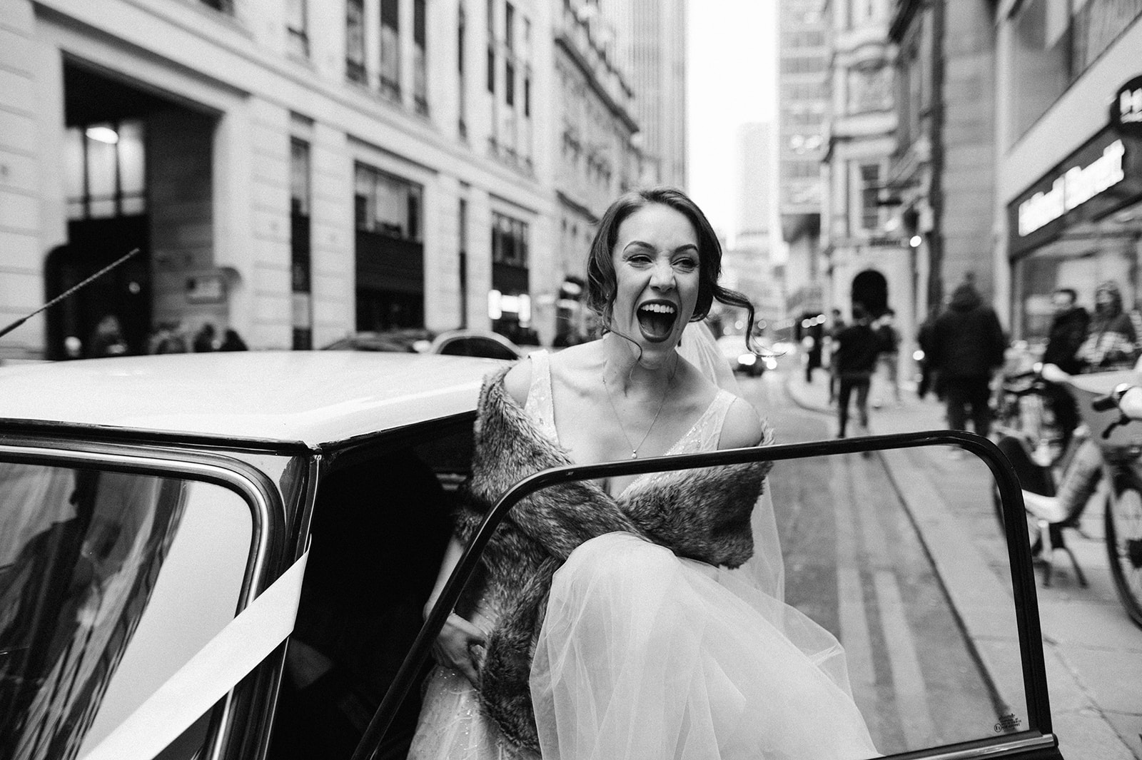Bride laughing as she gets into their mini wedding car in London